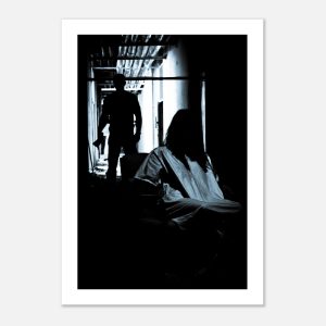 Dark black and white photograph of a seated woman and a shadowy figure in a corridor