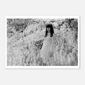 Young, mysterious woman in a flowing white dress amidst lush grass